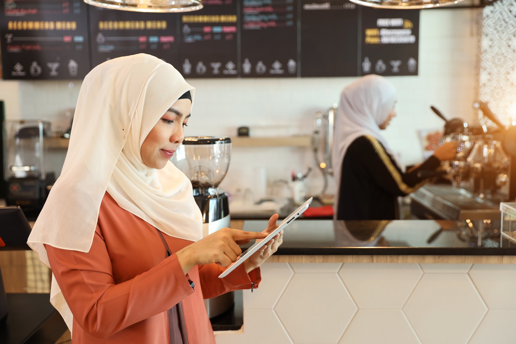 Hospitality founder checking orders on a tablet at her cafe counter